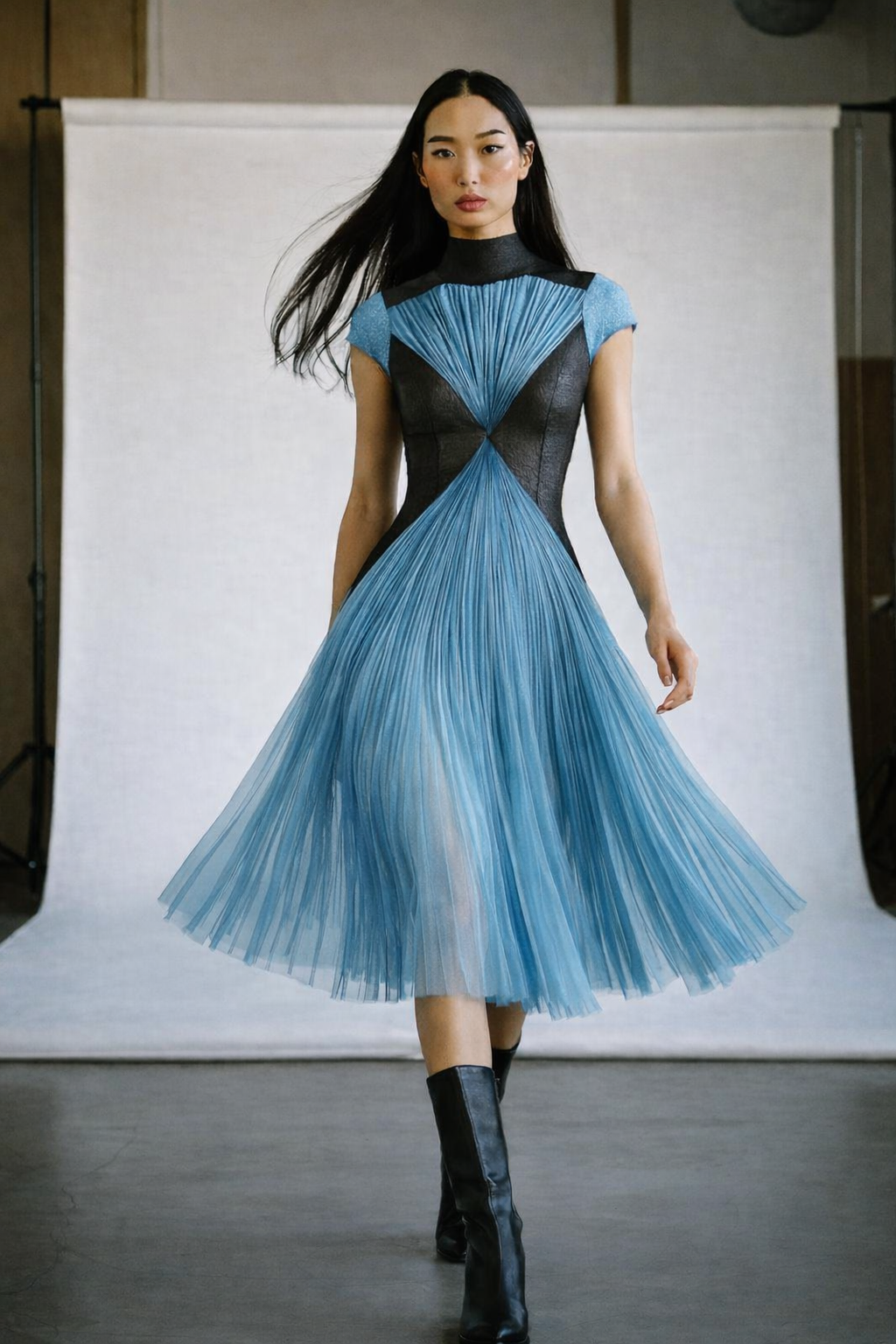 Mannequin portant une robe originale en tulle turquoise, manches courtes, jupe ample au genou, corsage noir en V soulignant la taille.